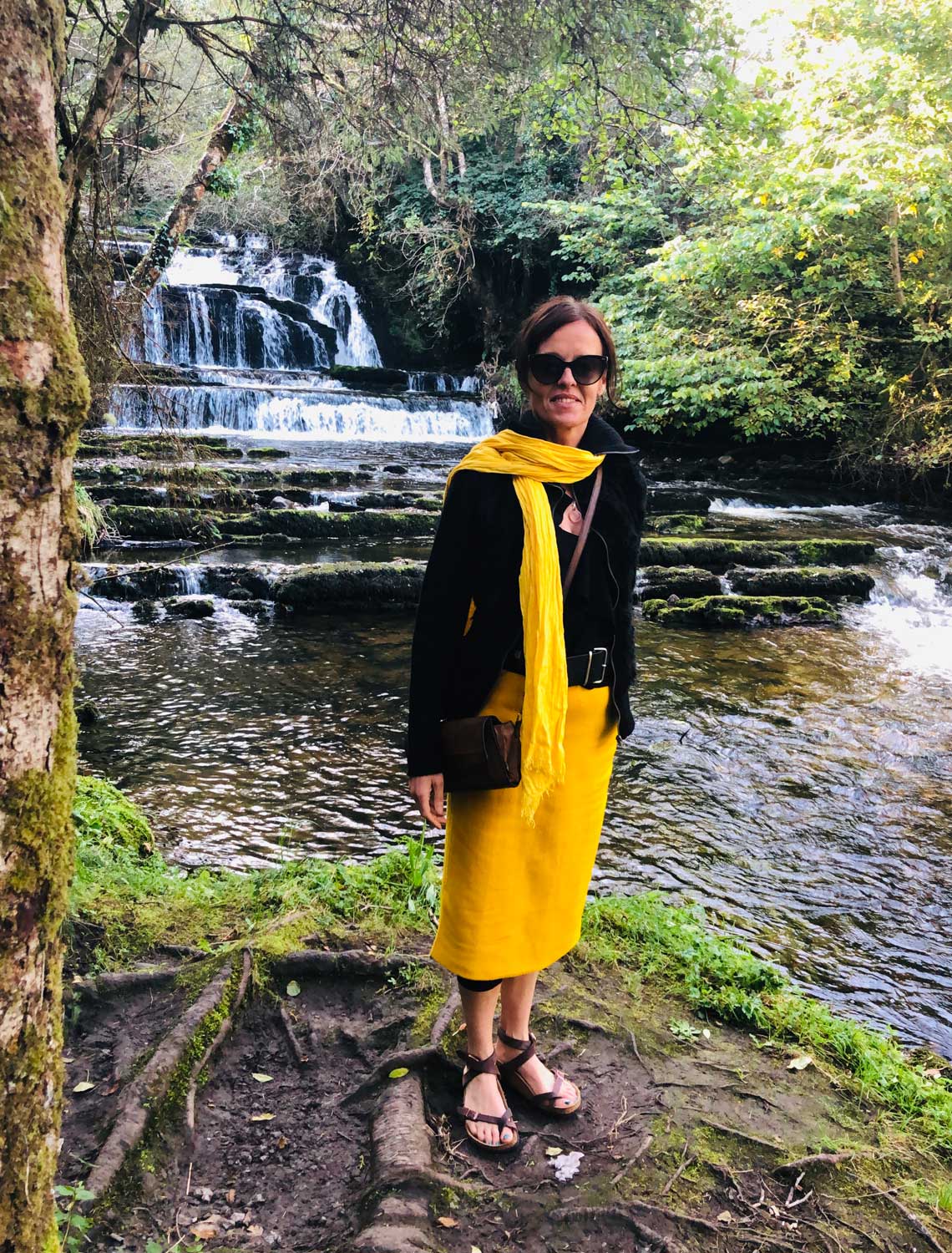 Finola in a wooded area surrounded by nature and standing in front of a waterfall
